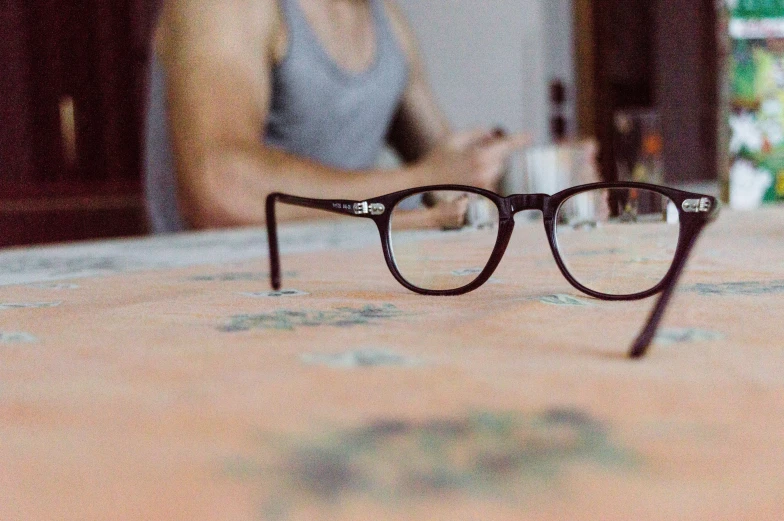 a pair of glasses laying on a table with a woman looking in the background