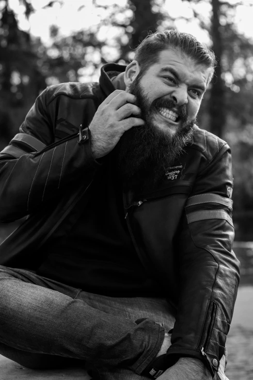 man smiling and sitting in the park, with his hands on his pockets