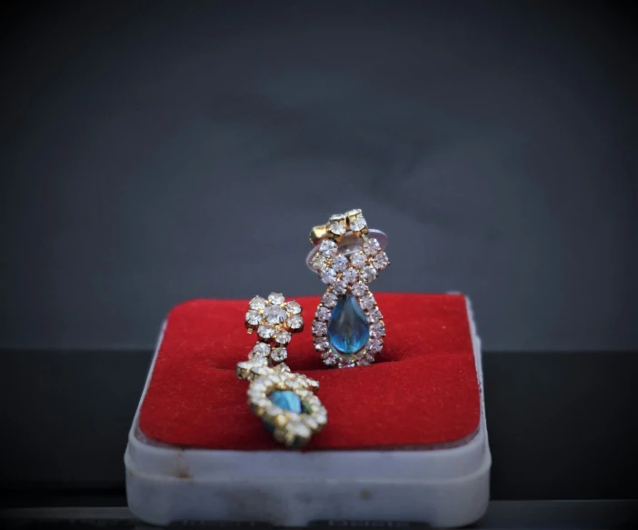 two engagement rings with a blue stone on top of a red velvet ring box