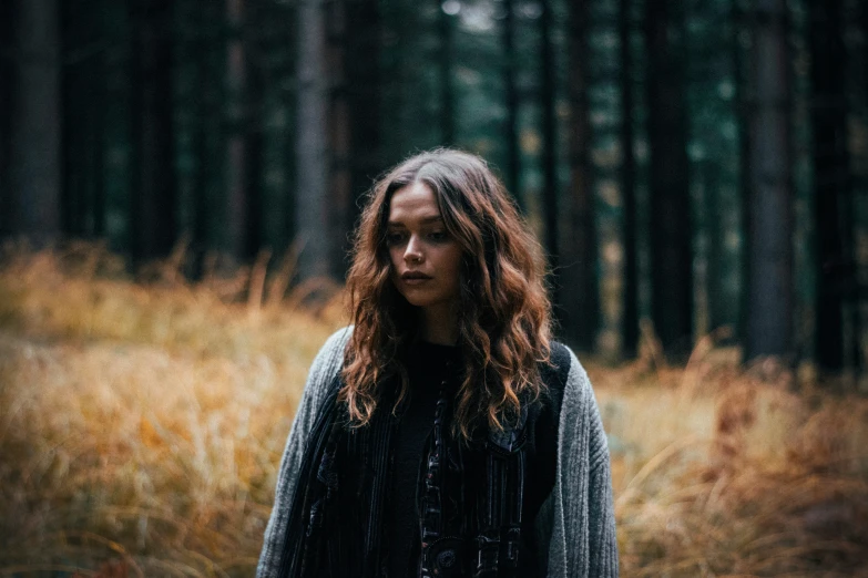 a person with long hair standing in front of a forest