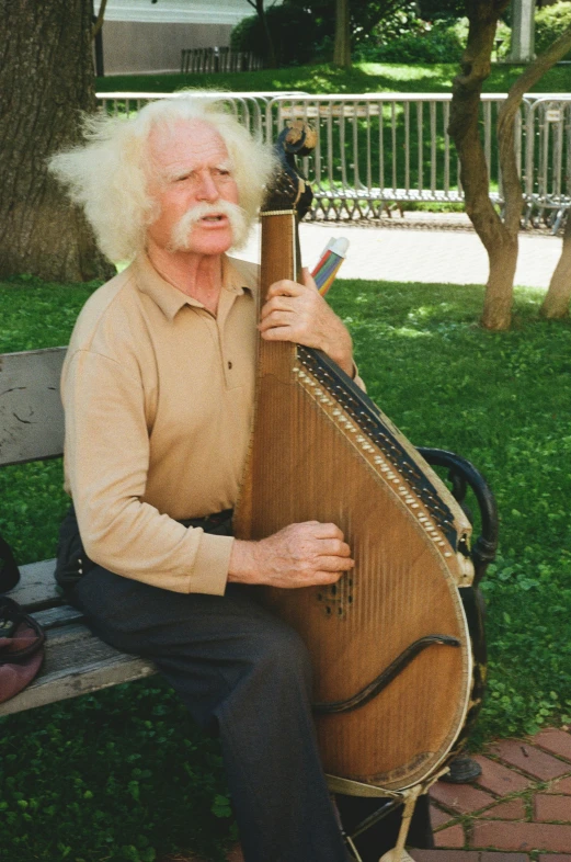 an older man sitting on a bench holding a large harp