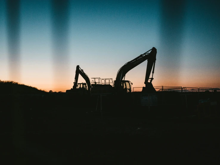 the silhouette of two large oil pumps at dusk