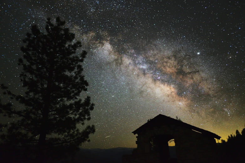 the night sky is lit up over a cabin on a mountain