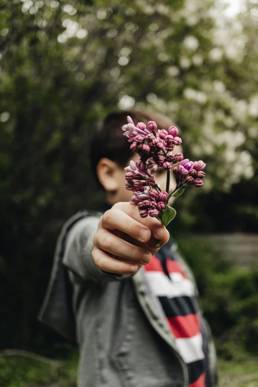 a man standing in front of trees and holding a pink flower