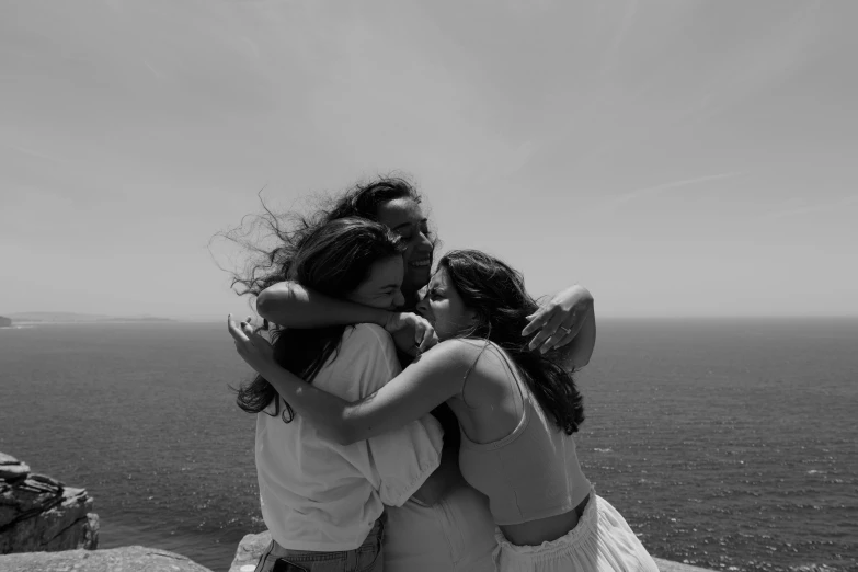 a group of three girls hugging and kissing on the edge of a cliff