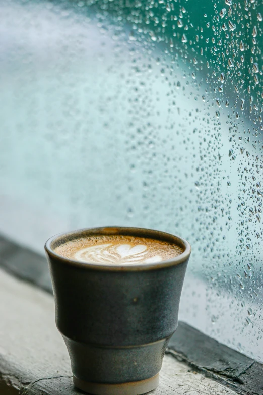 a close up of a cup on a window sill with drops of water behind it