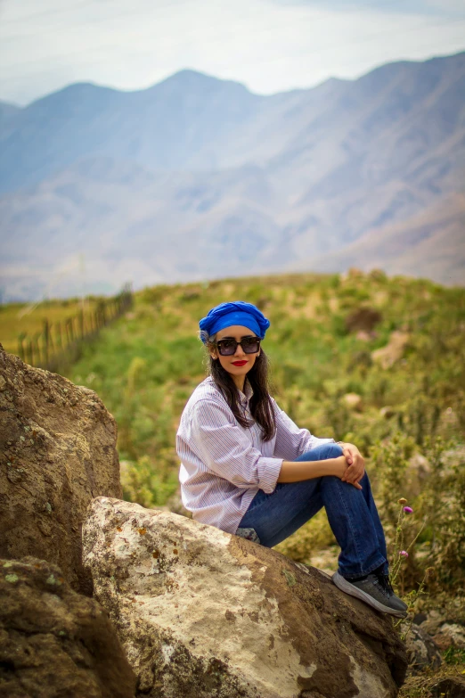 a beautiful young lady sitting on top of a rock