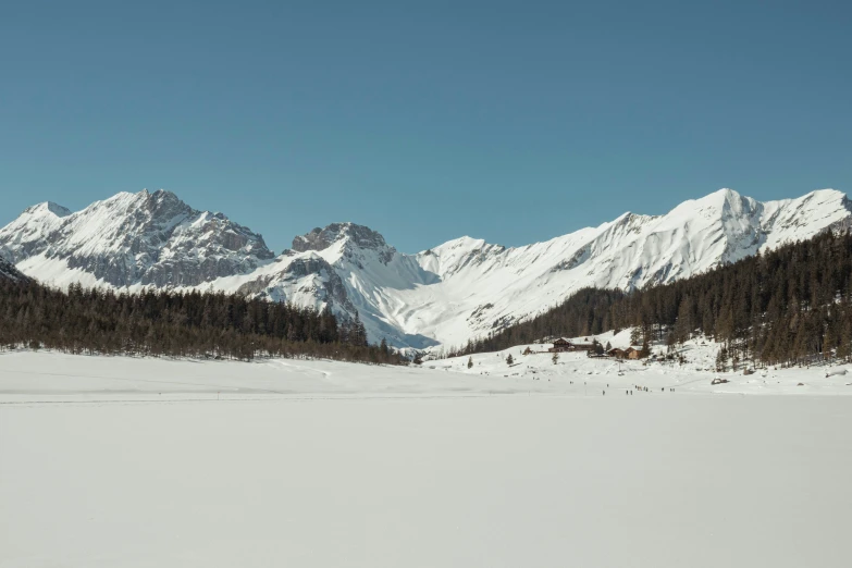 the mountains behind the snowy field are covered with snow