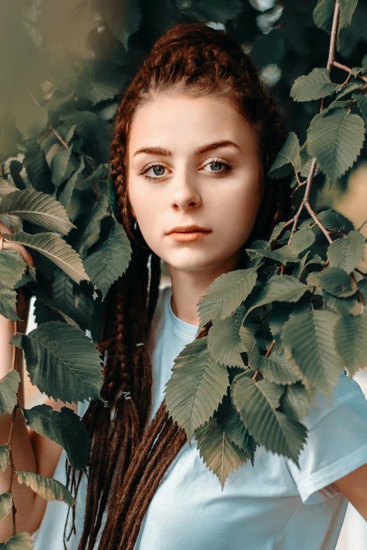 a woman with blue eyes is standing between a tree and leaves