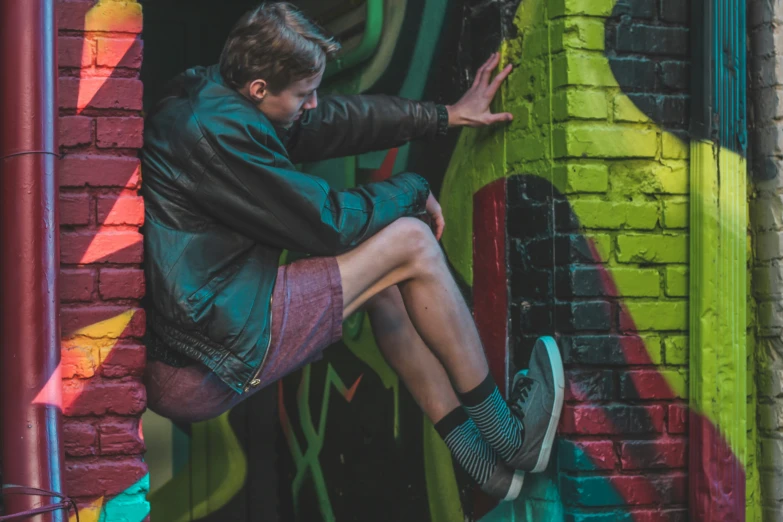 the man is sitting up against the graffiti covered wall