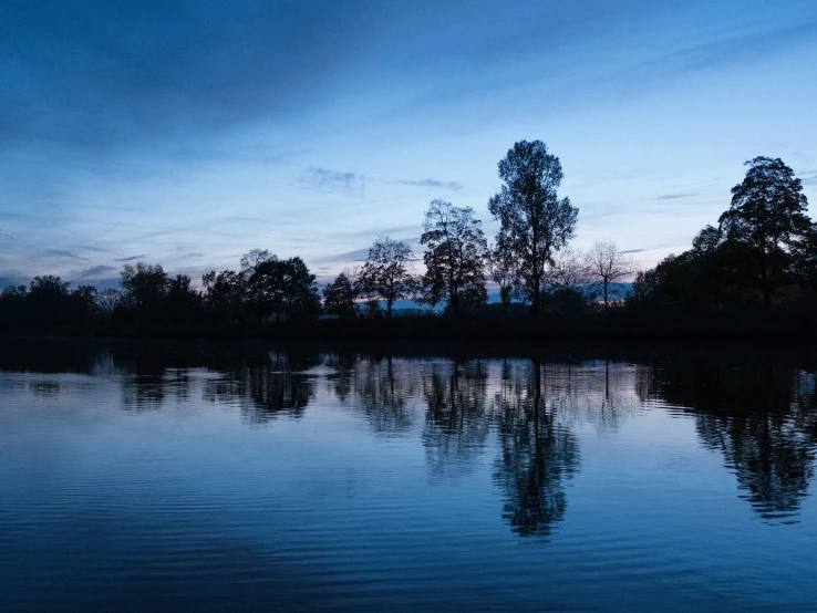 calm water and trees are in the distance at sunset