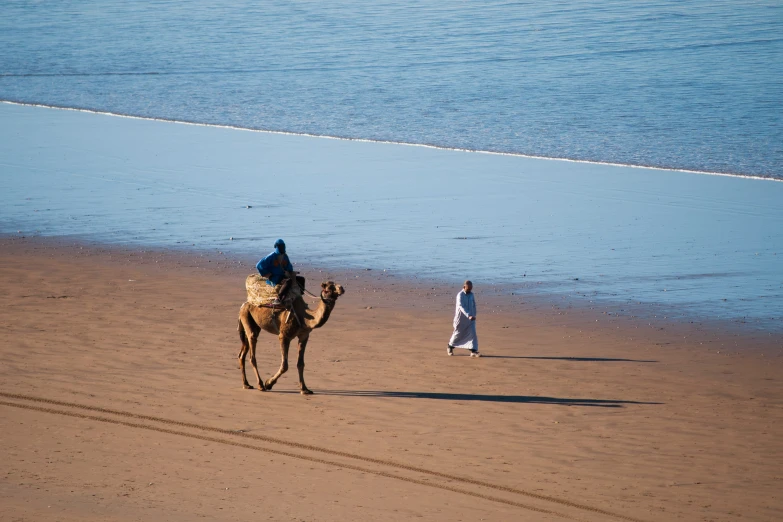 a man in a long white dress is walking a camel