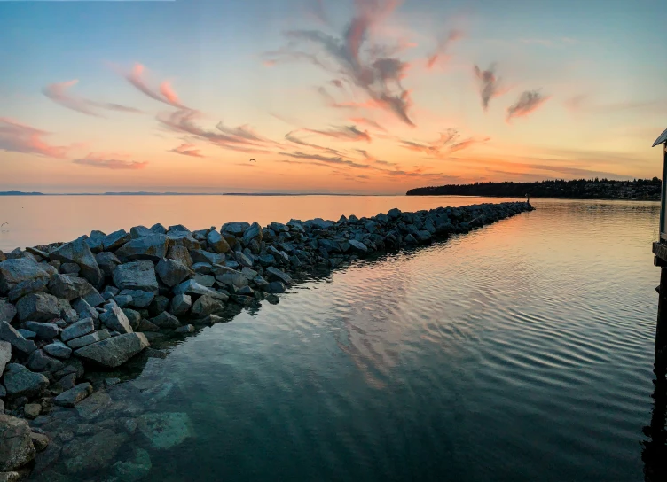 the sunset reflects on the water near a rocky shore