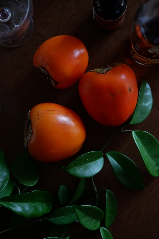 several tomatoes and leaves with some wine on a table