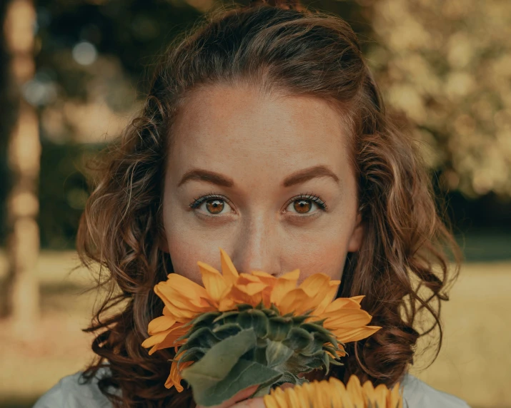 a woman with brown hair and blue eyes holding onto a sunflower