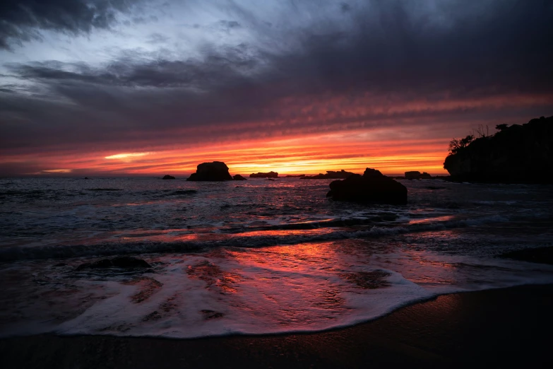 the sun sets at an ocean shore with small rocks in the foreground