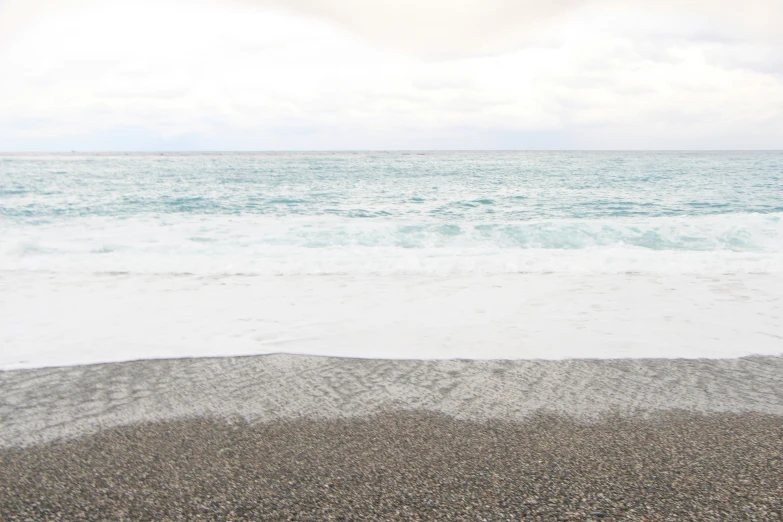 a lone bird standing in the sand next to an ocean