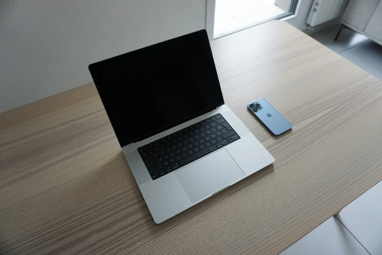 a laptop on the desk with a phone beside it