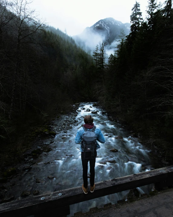 a man standing on a wooden railing next to a creek