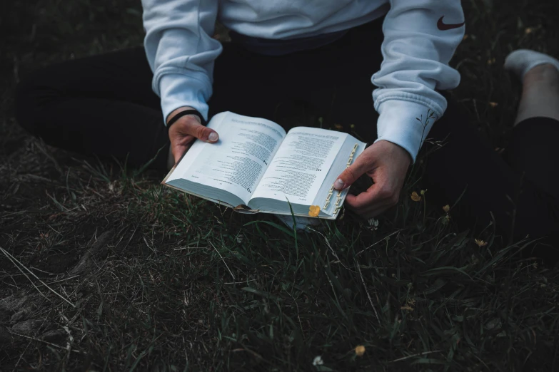 a person is sitting in the grass holding a book