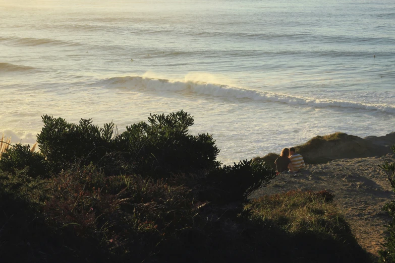 there are people sitting and watching the waves come in