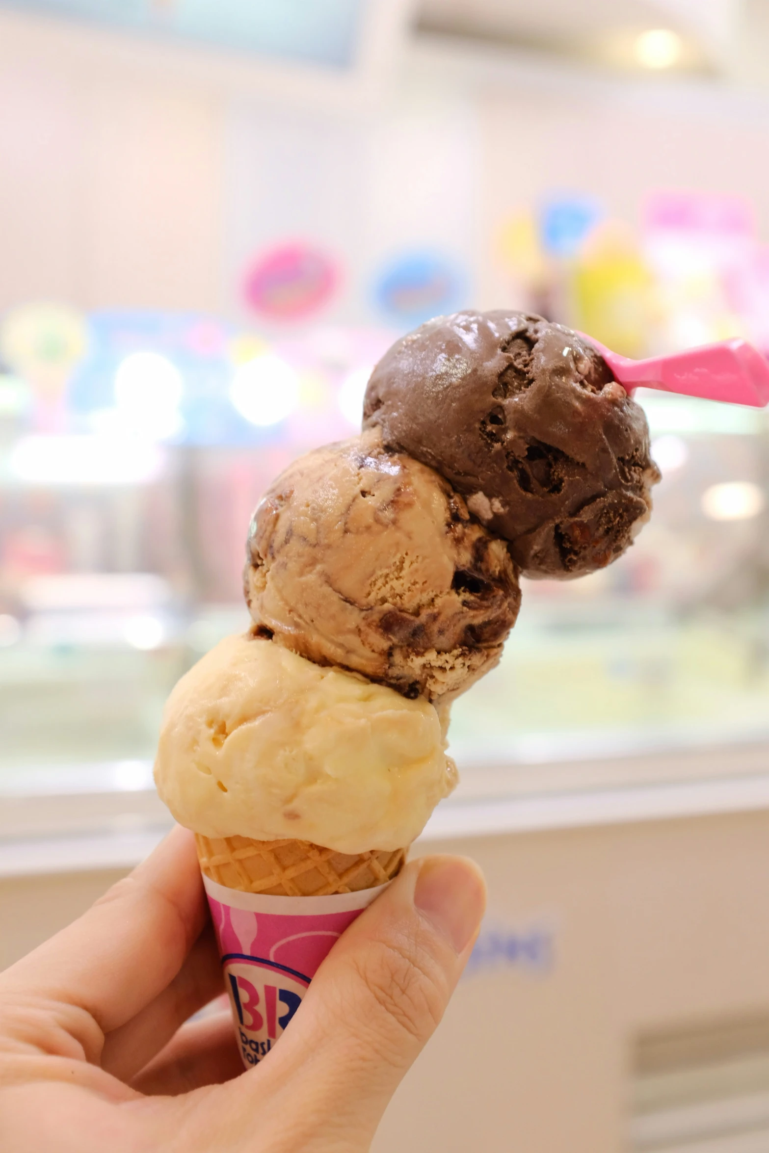 someone's hand holding an ice cream cone in front of a window