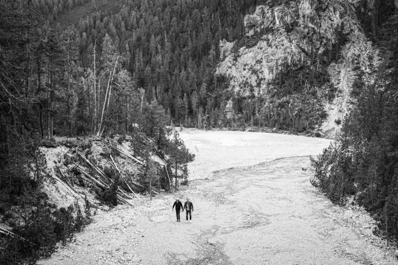 two people are walking in a narrow road in the woods