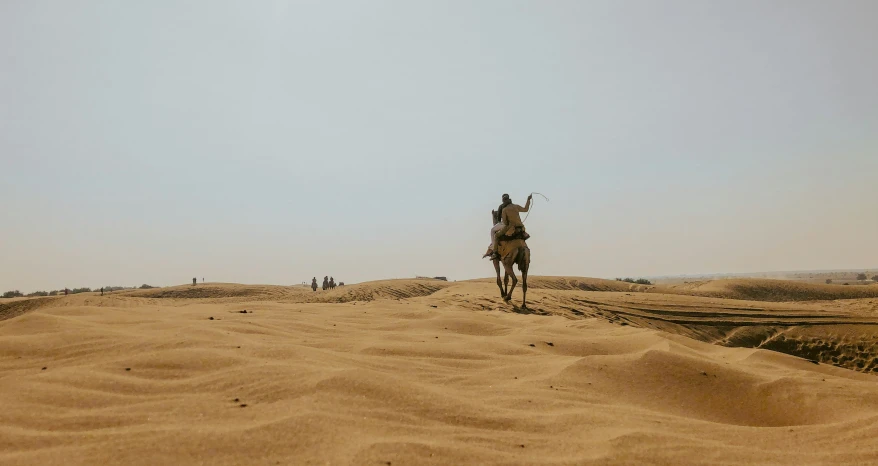 man riding on top of a horse over a sandy field