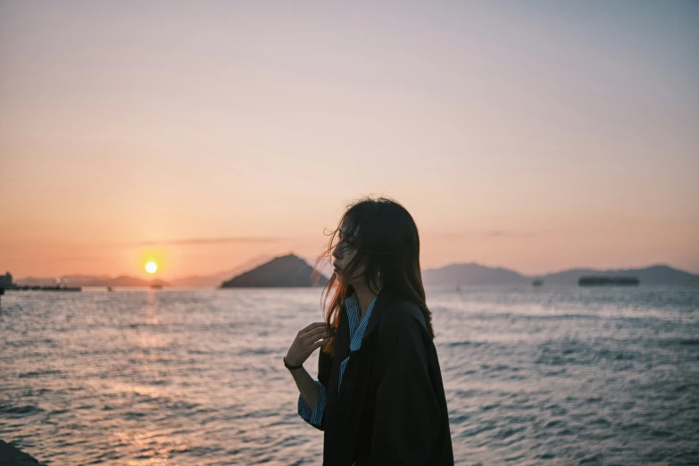 a woman stands on a beach and watches the sunset