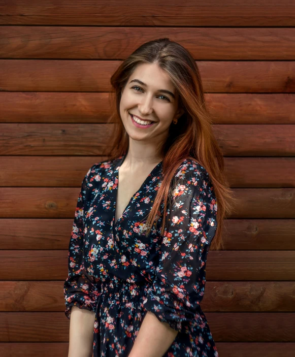 a smiling woman leaning against a wooden wall