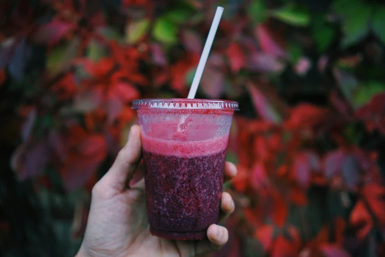 a hand holds a smoothie with a straw and purple stuff