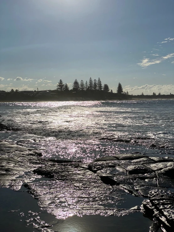 the sun shining on an ocean with trees behind it