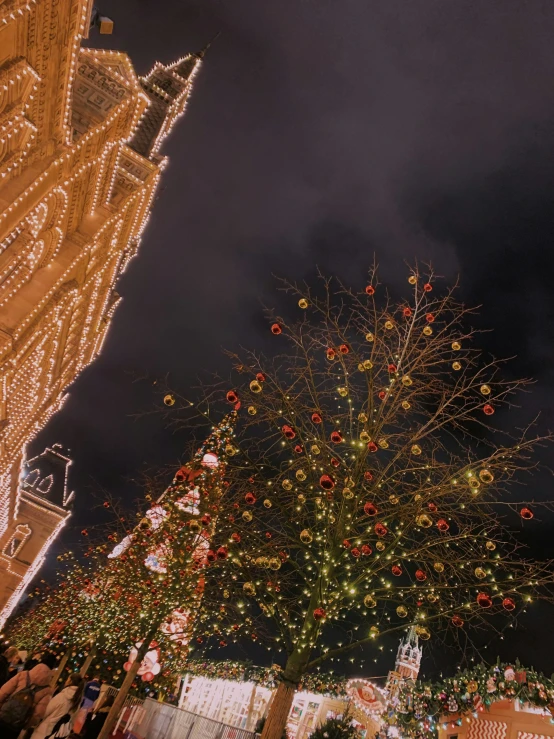 a very large christmas tree with lights near many buildings