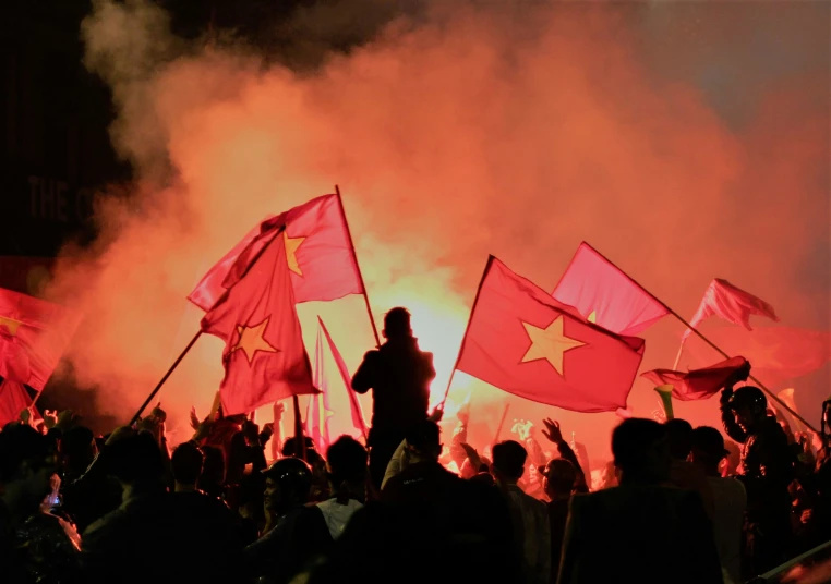 people waving flags at night with a lot of smoke coming out