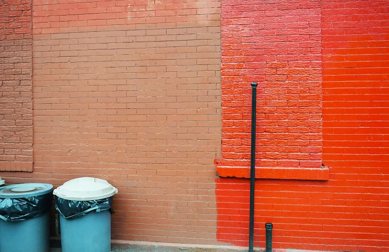 trash cans line the curb next to an orange wall