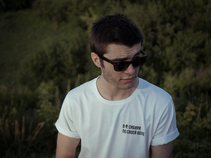 a man in sunglasses is standing near some bushes