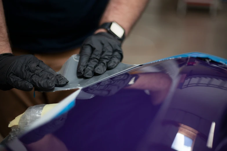 a person wearing black gloves  and waxing up a purple car