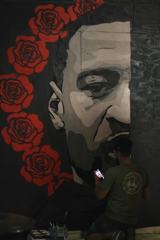 a man in green shirt painting a wall with flowers on it