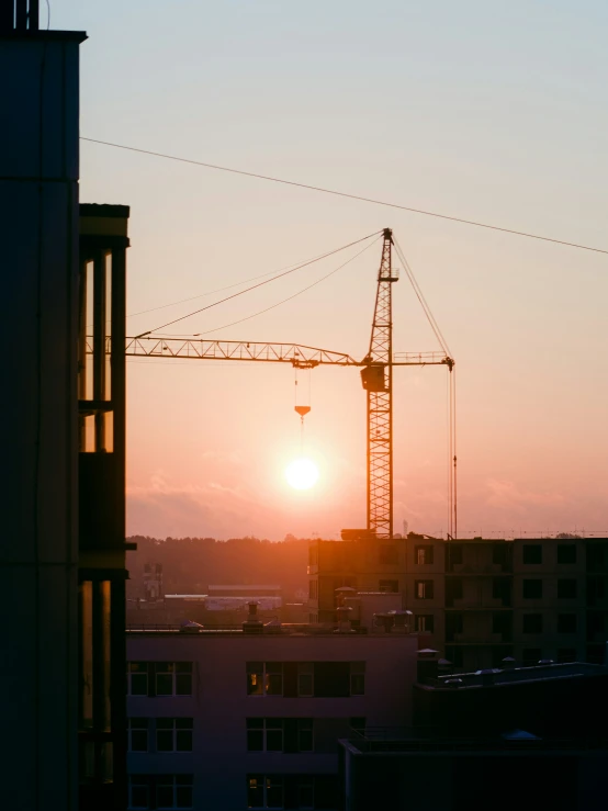 there is a tower crane at sunset behind buildings