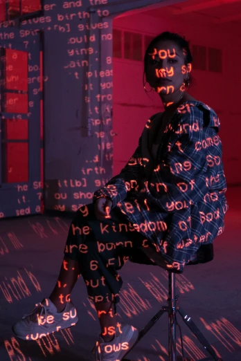 a person with text projected on their face and head, sitting on a stool