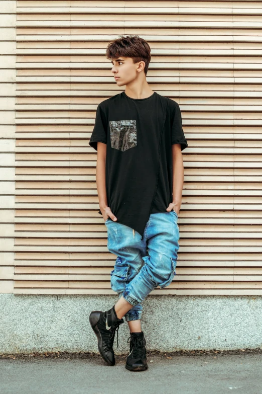 a person wearing black shirt with ripped jeans and black boots standing in front of a wall