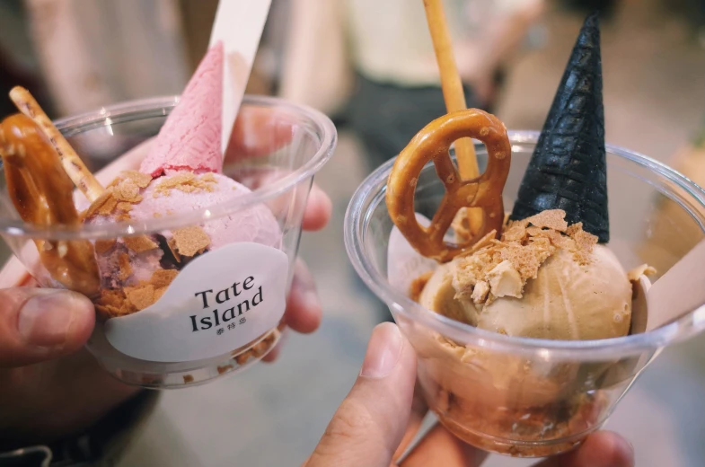 people are holding plastic cups with ice cream and pretzel