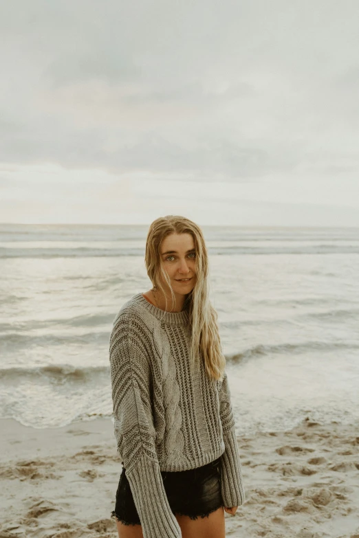 a woman posing on the beach with her hands in her pockets