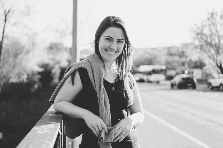 woman smiling for the camera sitting on a bench on the side of the road