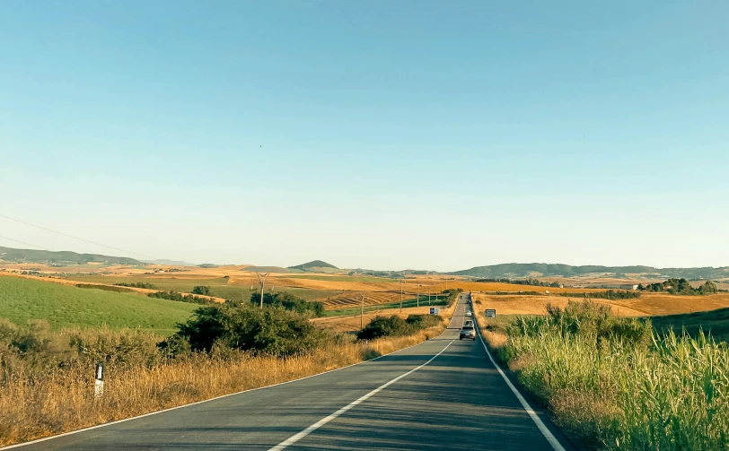 the view from the street of a long stretch of road with fields, hills and rolling hills