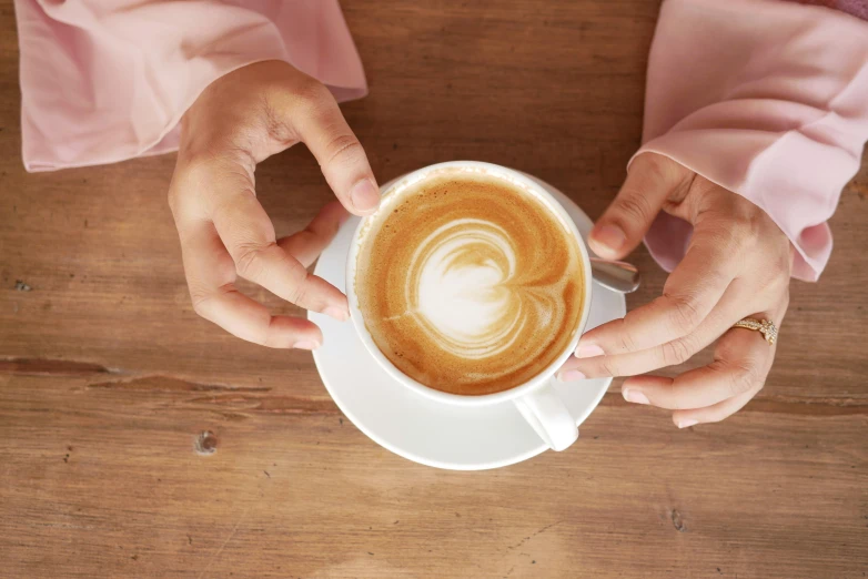 two hands on a white coffee cup filled with latte