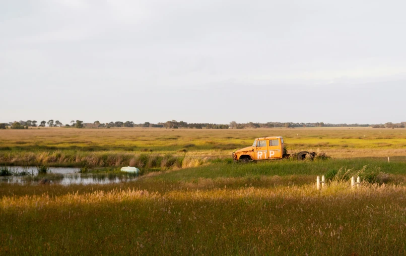 an orange truck in a field next to a pond