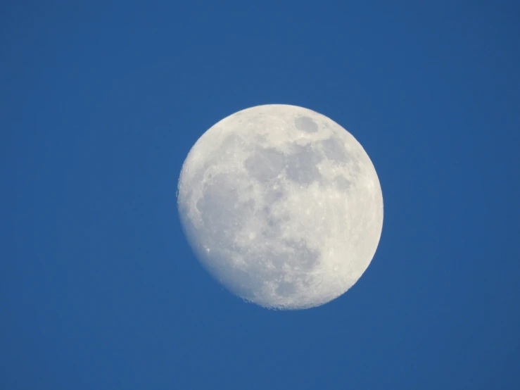 a full moon in the blue sky above it