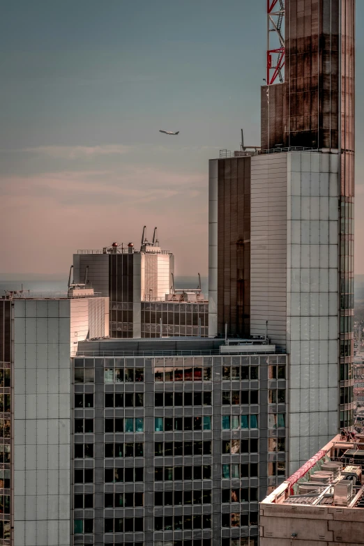 the skyline is very tall and grey as a plane flies over the skyscrs