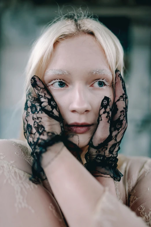 a blonde woman wearing black lace gloves with hands around her head